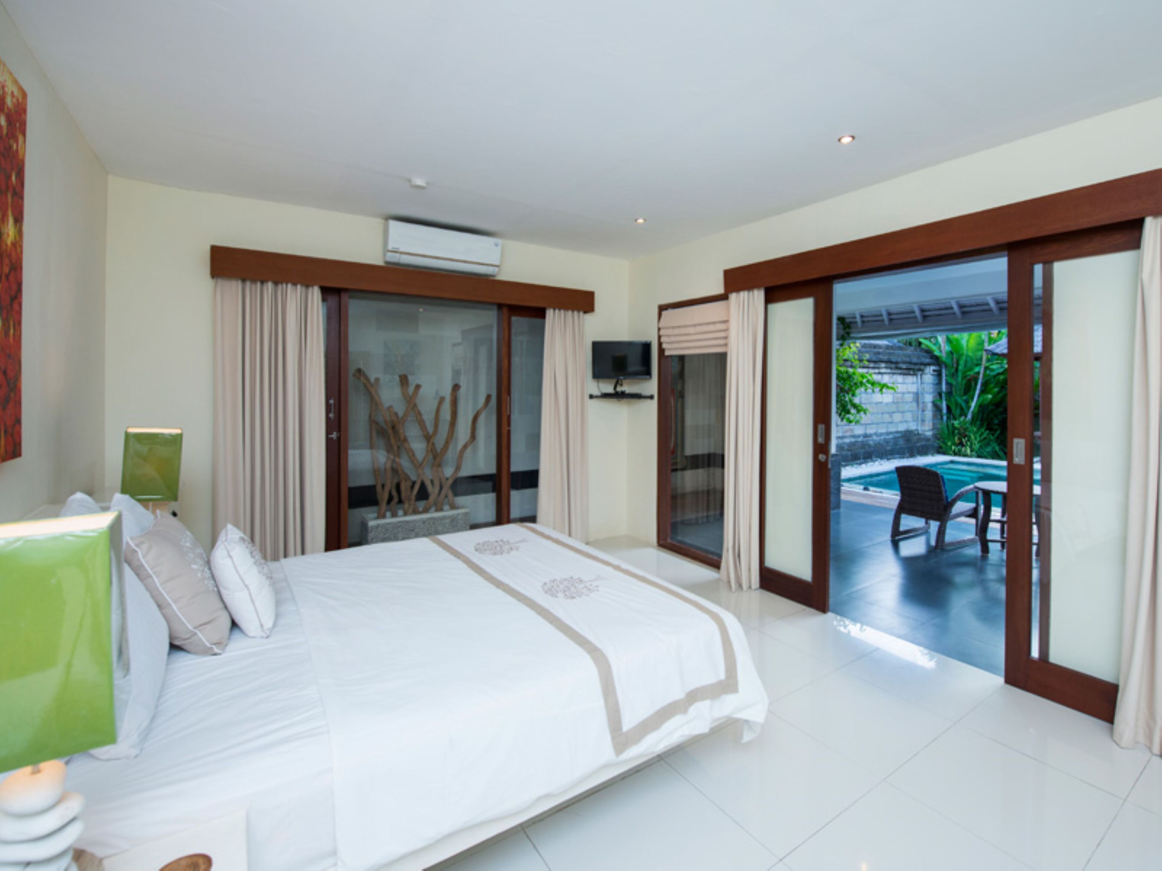 A spacious bedroom with a large bed, a TV, and a sliding glass door leading to a pool area.