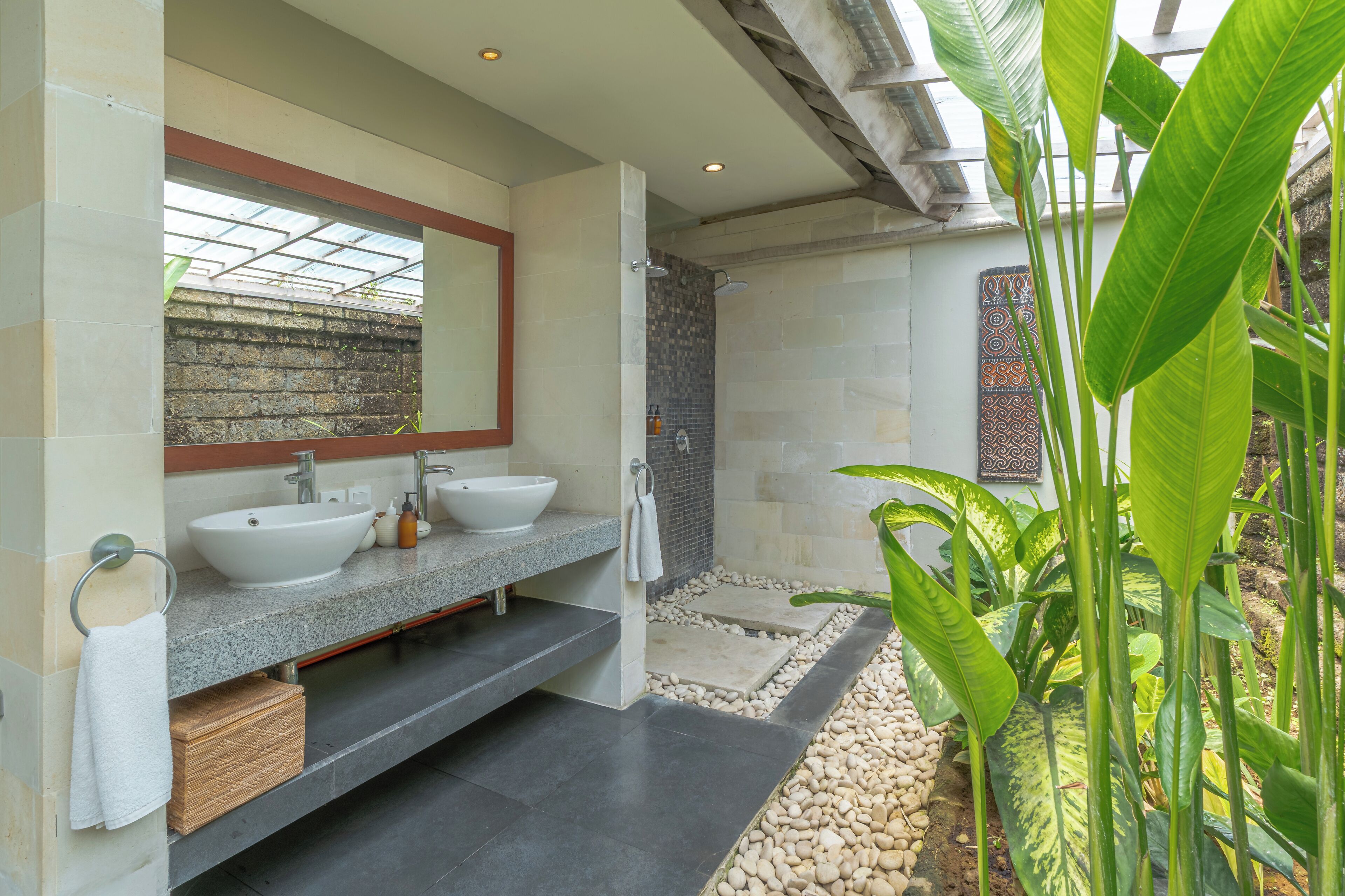 A modern bathroom with a large mirror, two sinks, a shower, and a small garden area with pebbles and plants.