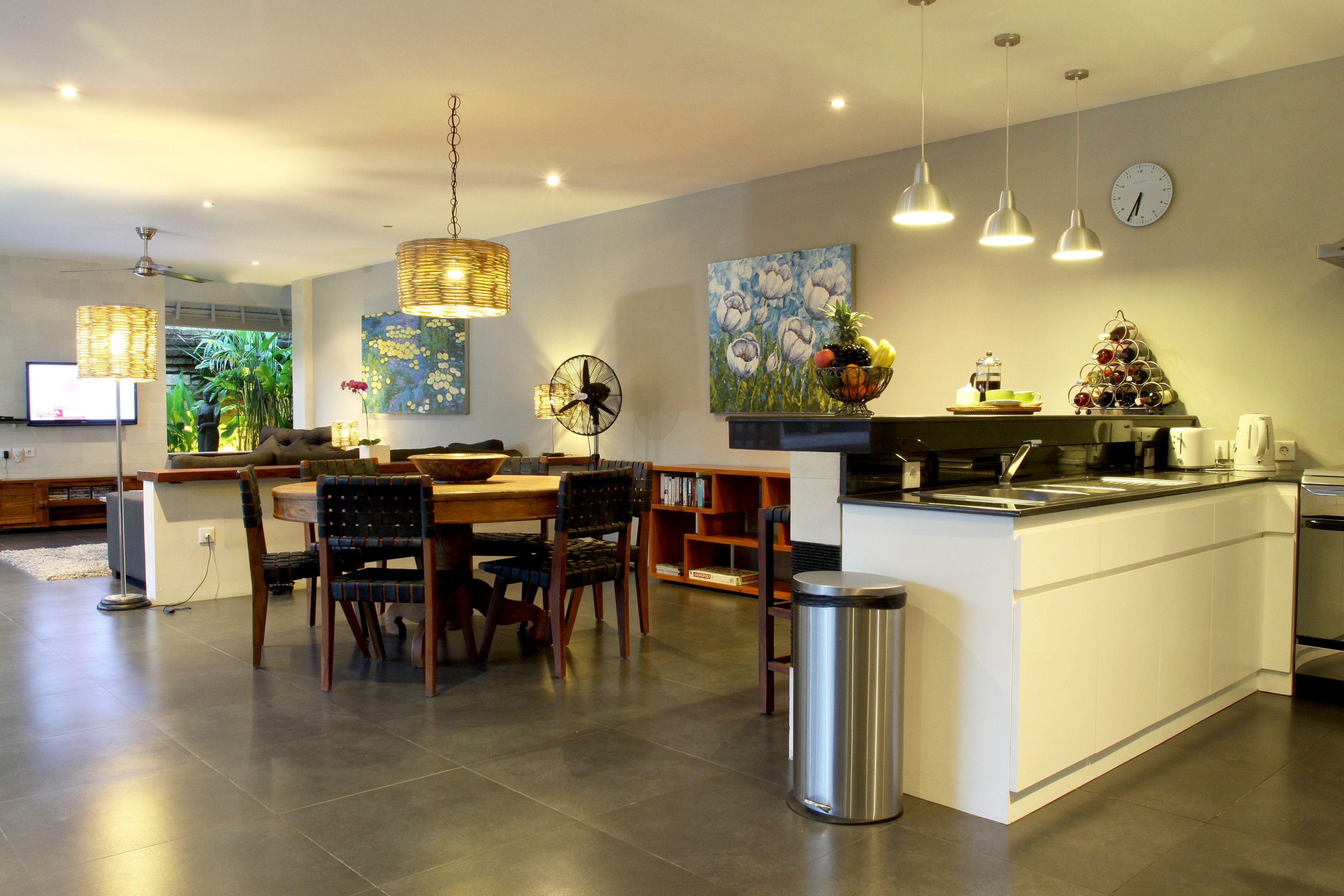 A modern kitchen with a central island, dining area with chairs, and a large window with plants.