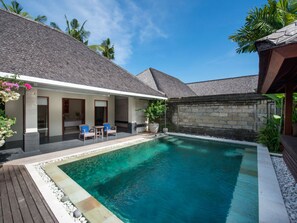 A swimming pool with a wooden deck, a covered seating area, and a stone wall. - Anyar Estate (Kerobokan)