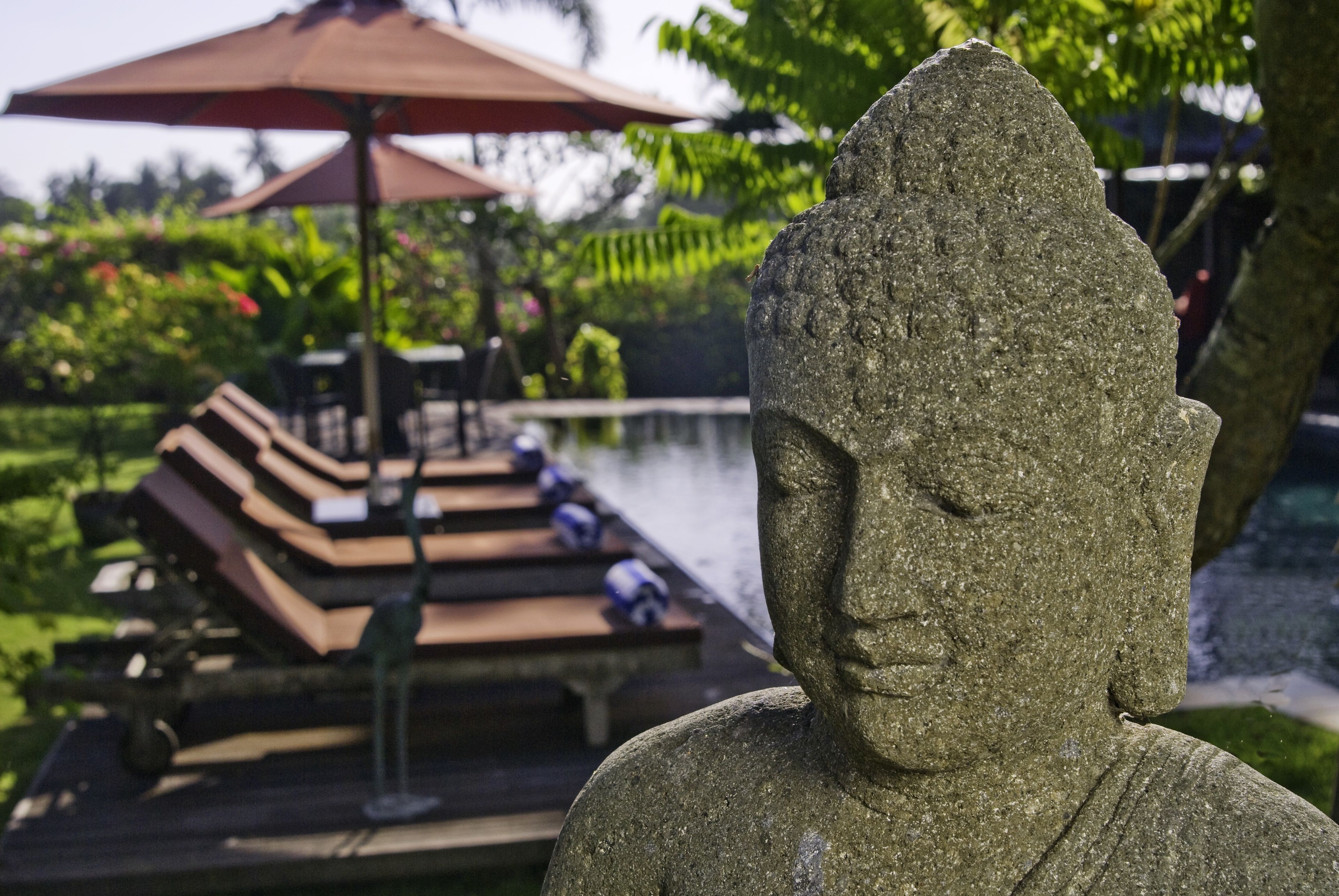 En sten Buddhastatue i en have med et bassin og liggestole.