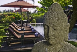 Estátua de Buda de pedra em um jardim com piscina e espreguiçadeiras.