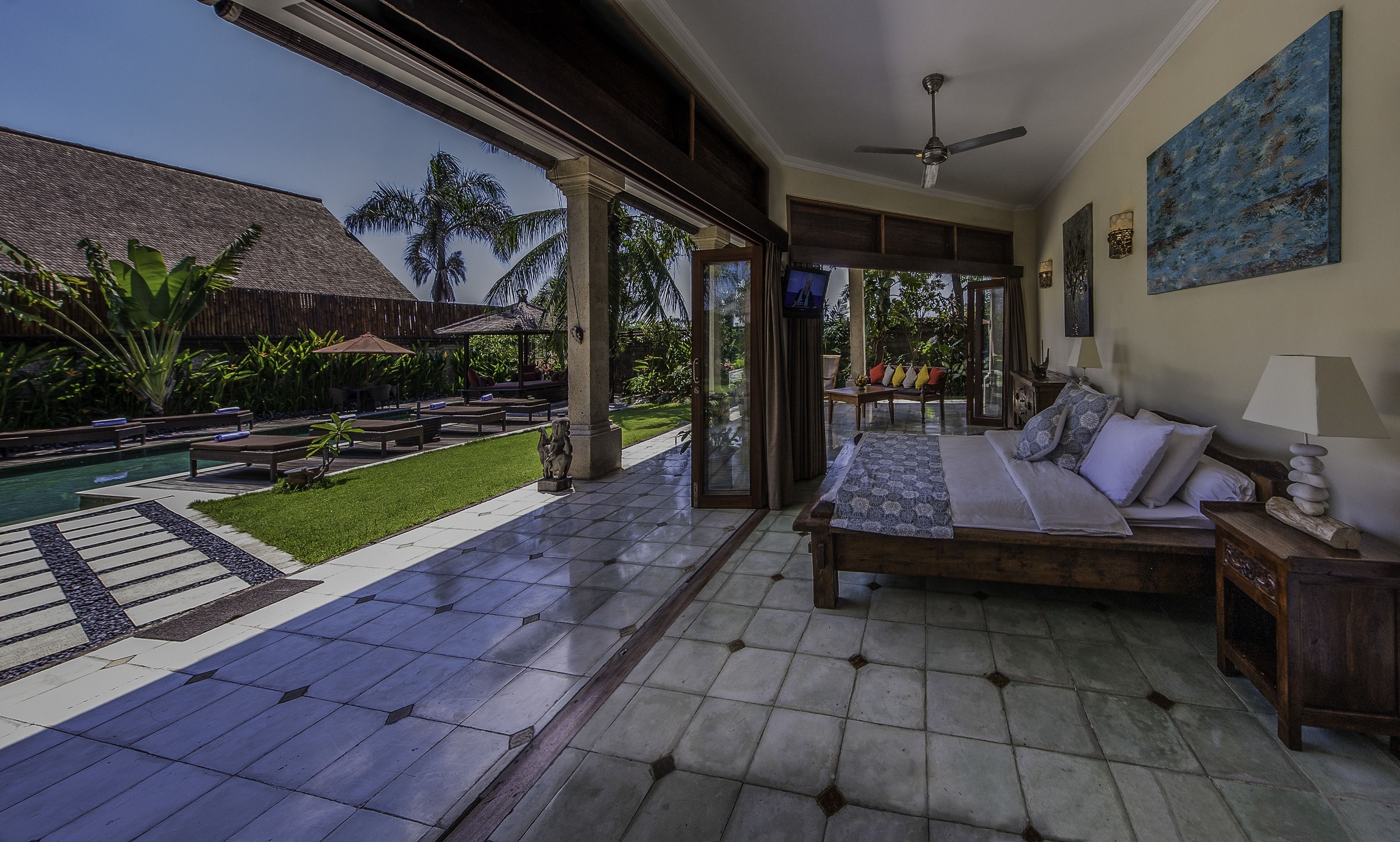 A bedroom with a bed, a TV, and a view of a pool and garden.