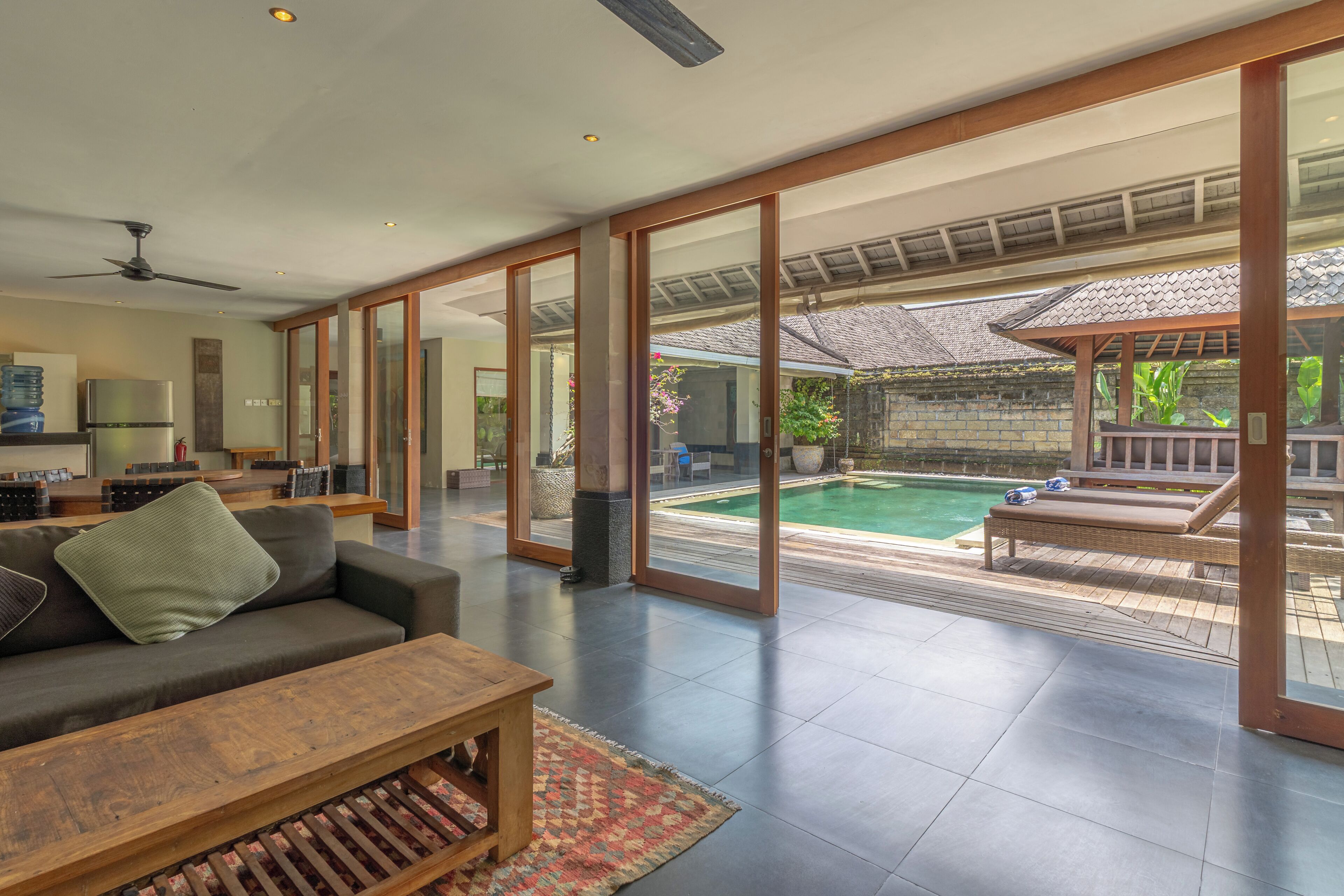 A spacious living area with a large sofa, a wooden coffee table, and a view of a swimming pool and outdoor seating area.