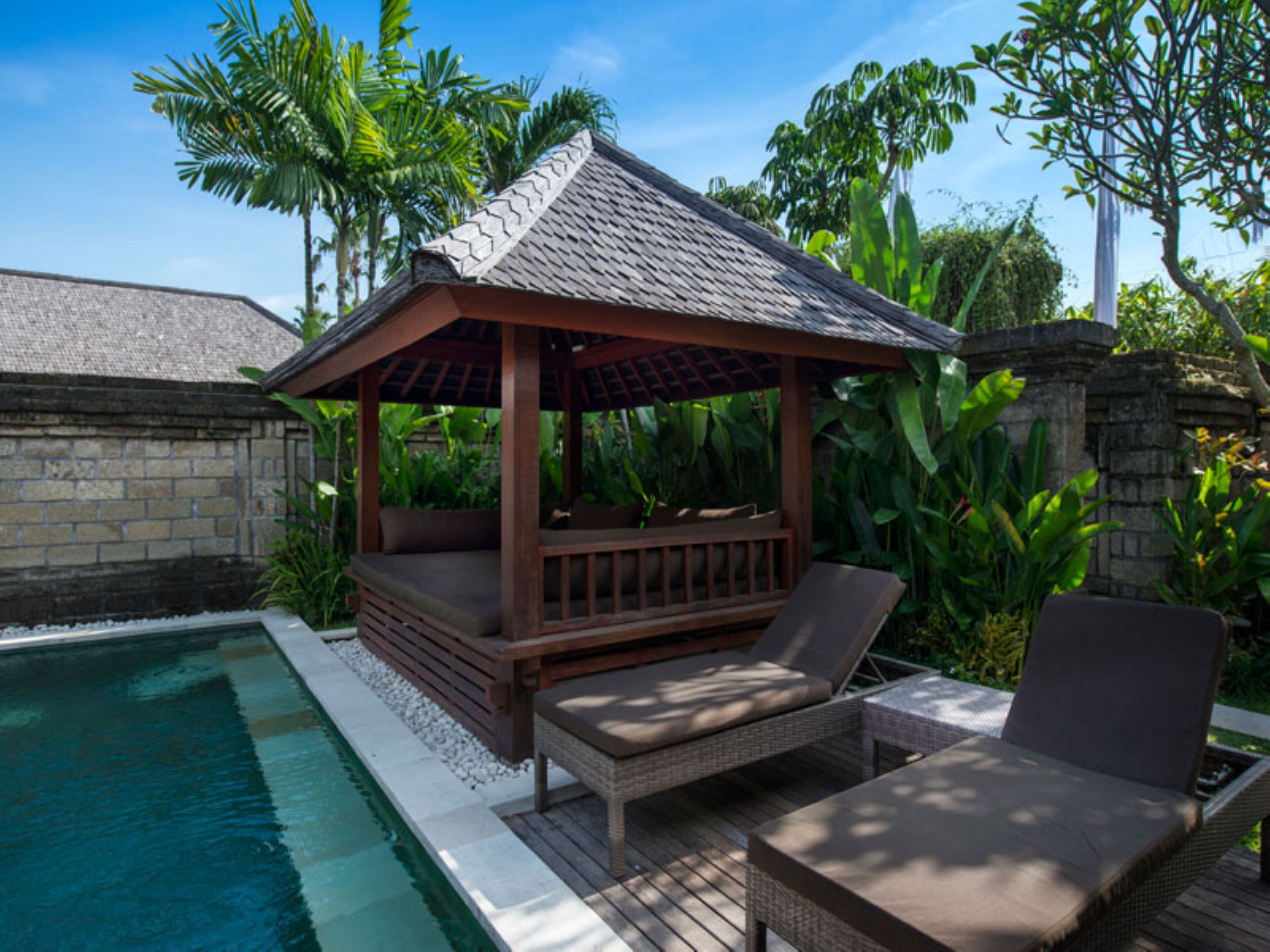 A poolside area with a gazebo, lounge chairs, and a stone wall.