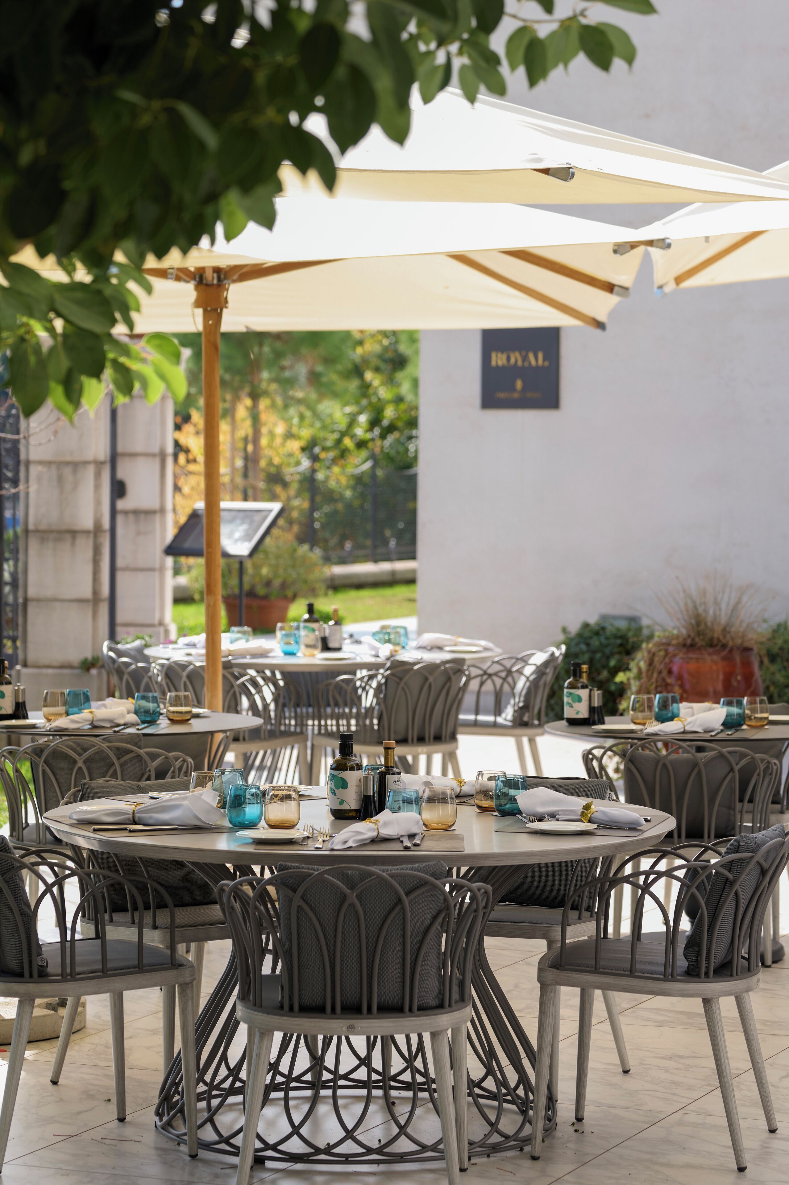 Un espace de restauration en plein air avec des tables et des chaises rondes, des parasols et une enseigne sur laquelle on peut lire « ROYAL ».