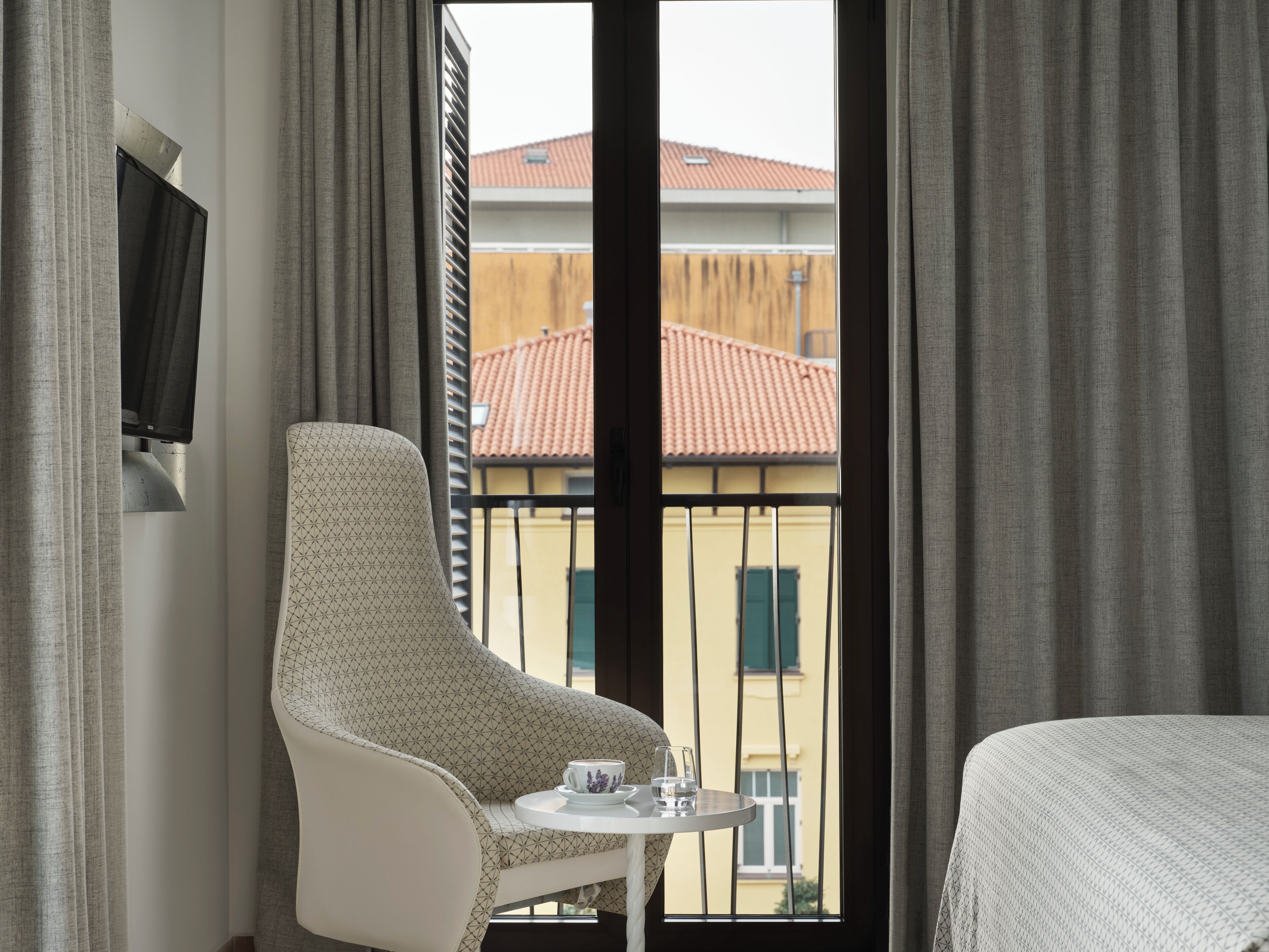 A hotel room with a large window, a sofa, a small table with a cup and glass, and a TV on the wall.