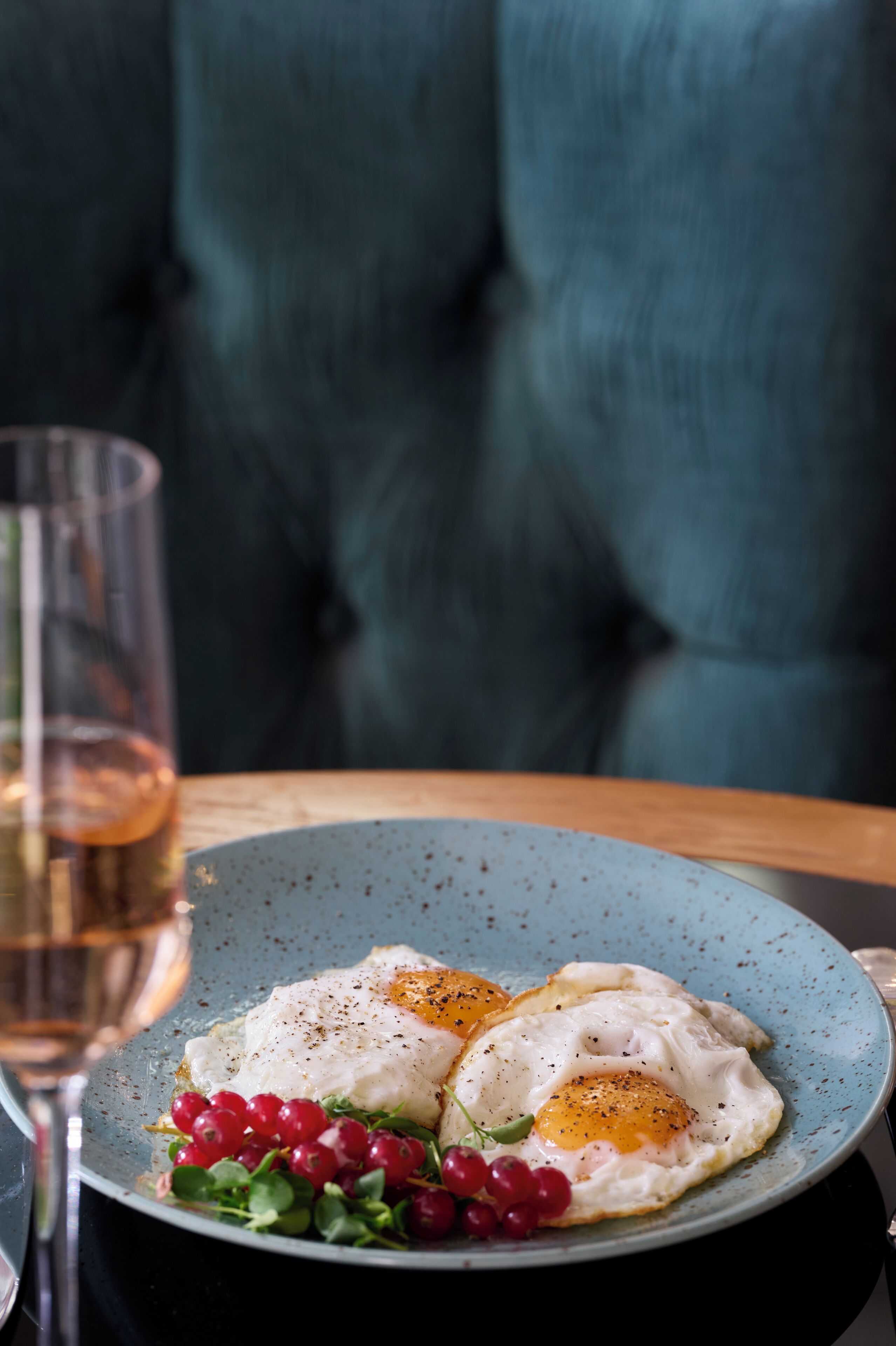 A plate with two sunny-side-up eggs, red currants, and greens on a blue plate.