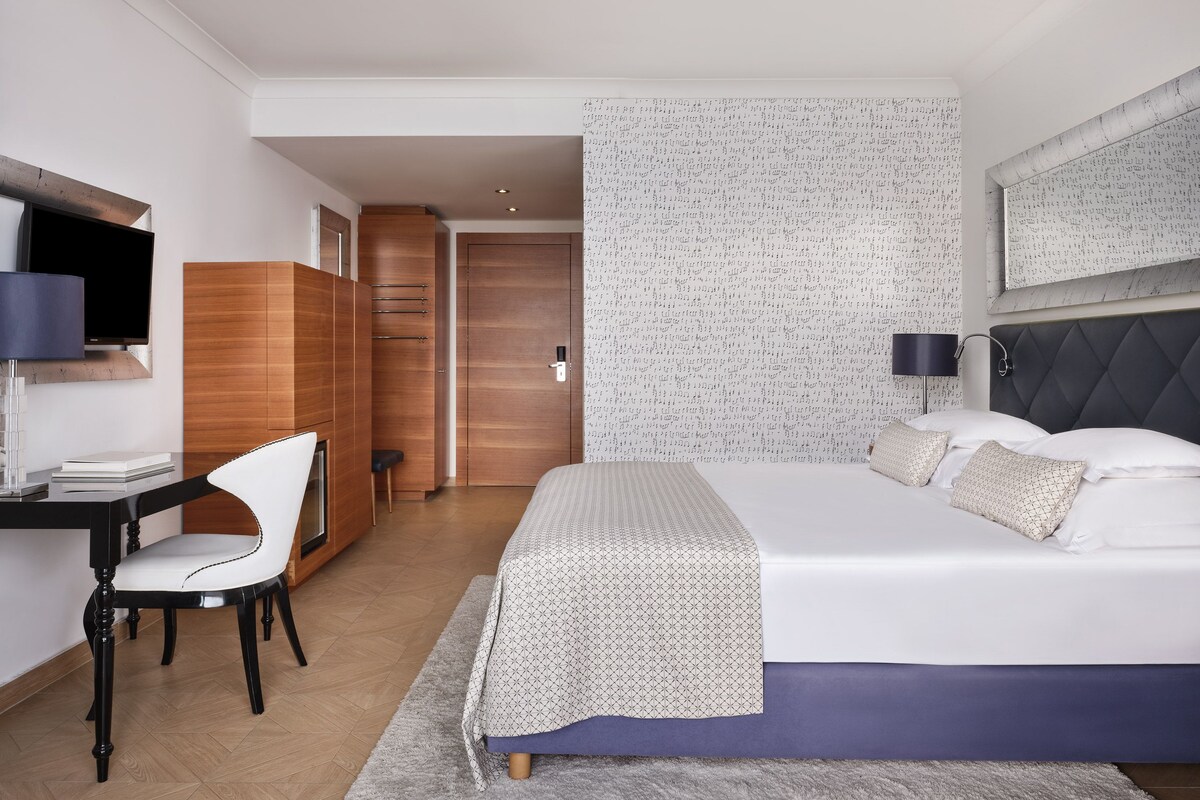 A modern hotel room with a bed, desk, chair, and wardrobe.