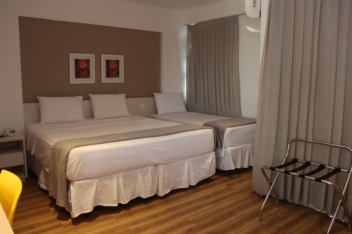 Een hotelkamer met twee bedden, een nachtkastje, een stoel en een raam met gordijnen.