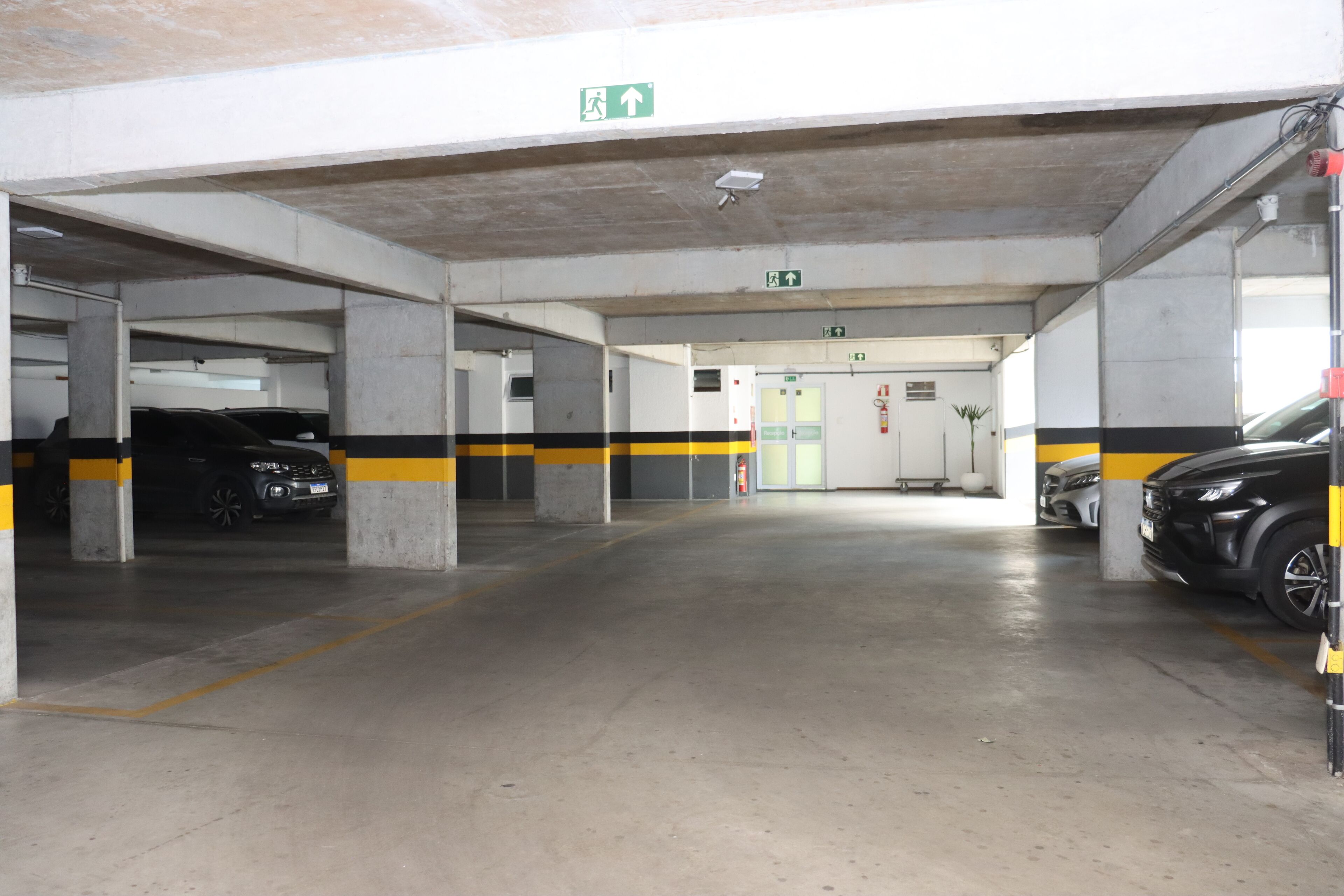 A multi-level underground parking garage with concrete pillars, yellow and black striped lines, and emergency exits.