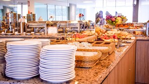 A buffet setup with various food items and stacked plates. - Único Apart Hotel (Feira de Santana)