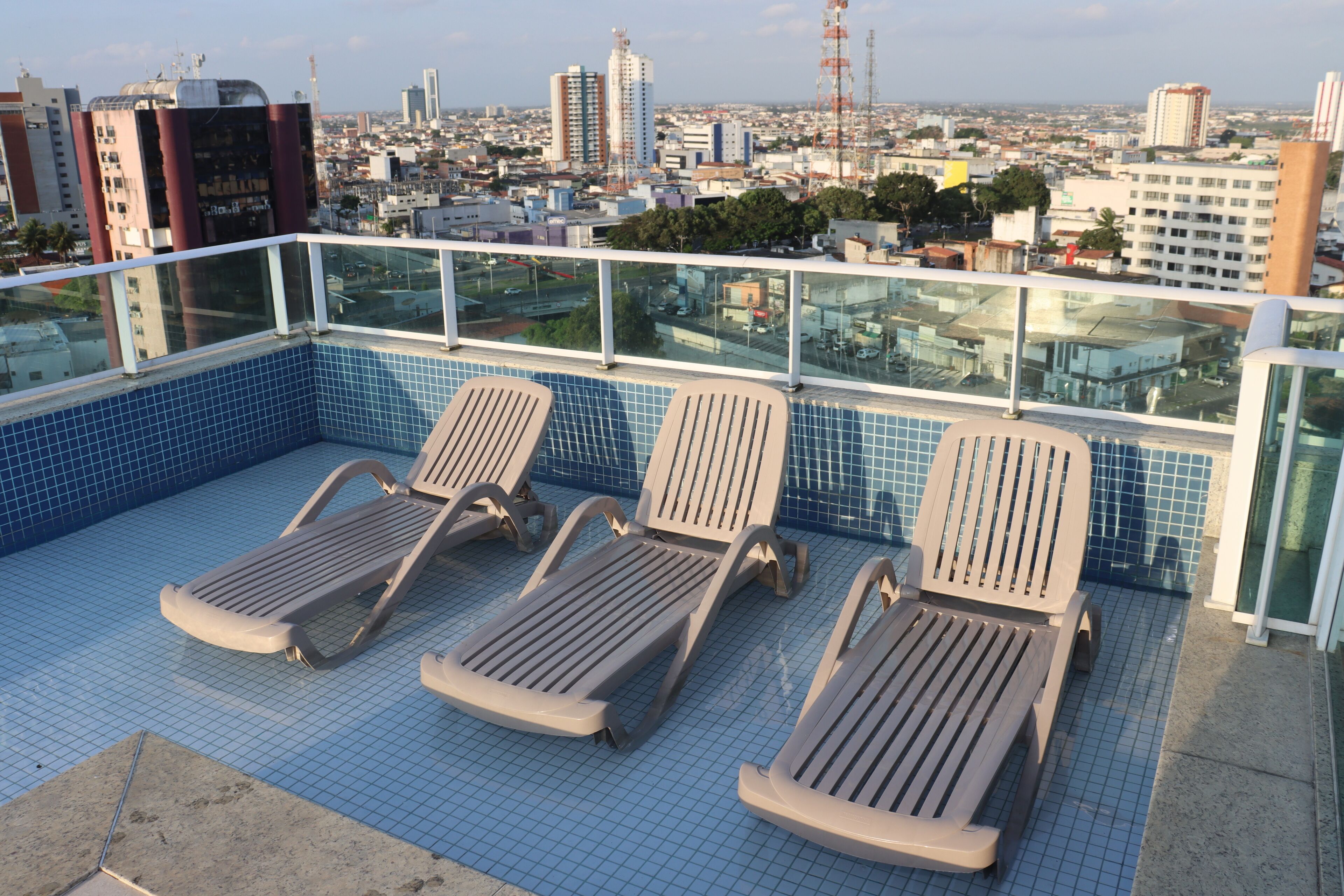 A rooftop pool with three sun loungers and a city view.