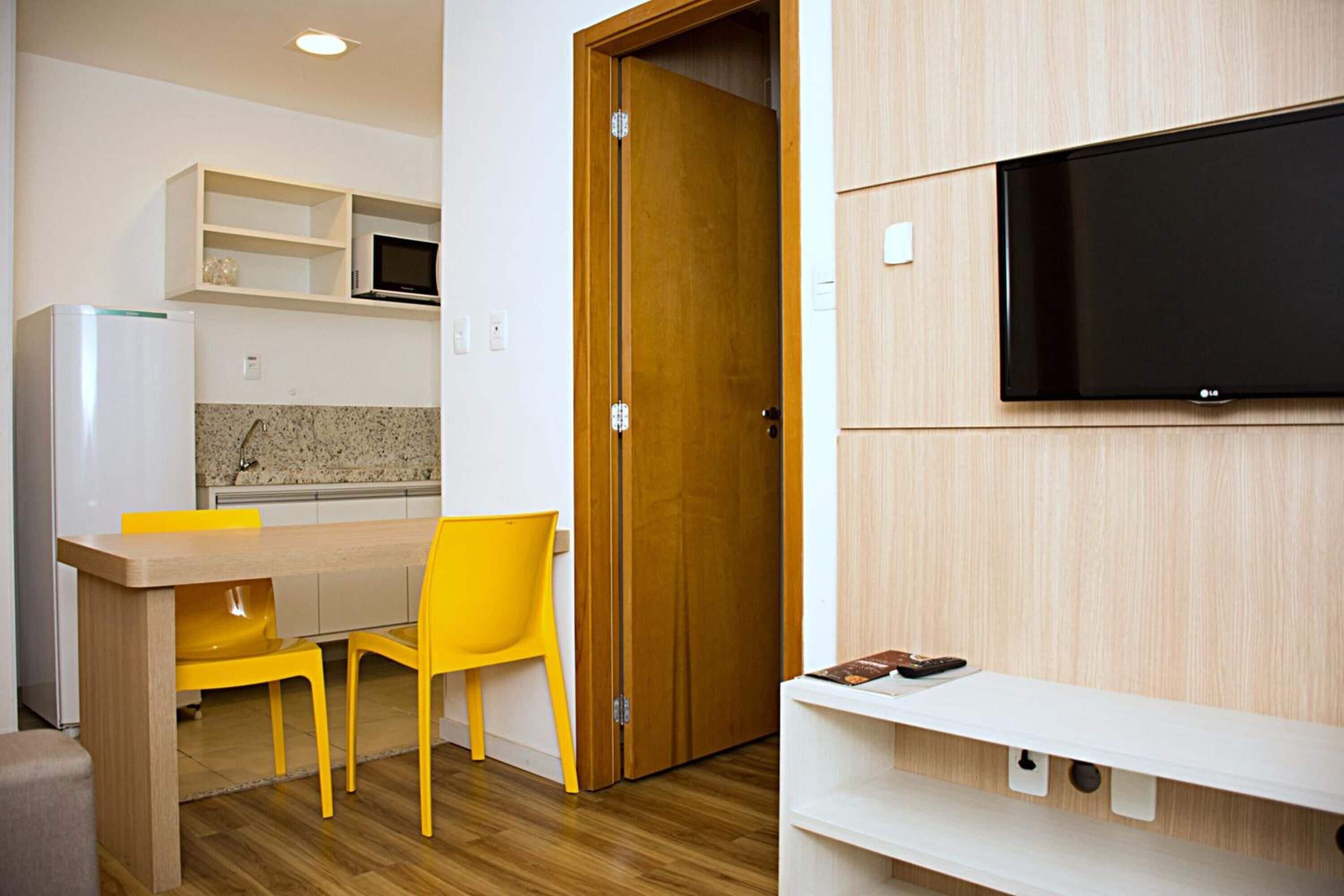 Een compacte keuken met een magnetron, een houten deur en een aan de muur bevestigde televisie.