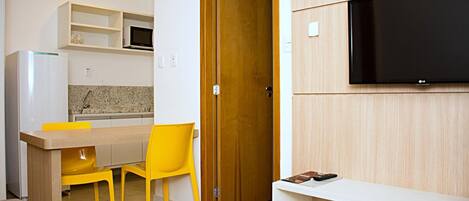 Een compacte keuken met een magnetron, een houten deur en een aan de muur bevestigde televisie.
