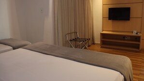 A hotel room with two beds, a TV mounted on the wall, a small shelf, and a window with curtains. - Único Apart Hotel (Feira de Santana)