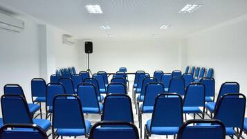 Un salón de conferencias con filas de sillas azules y un techo blanco con iluminación empotrada.