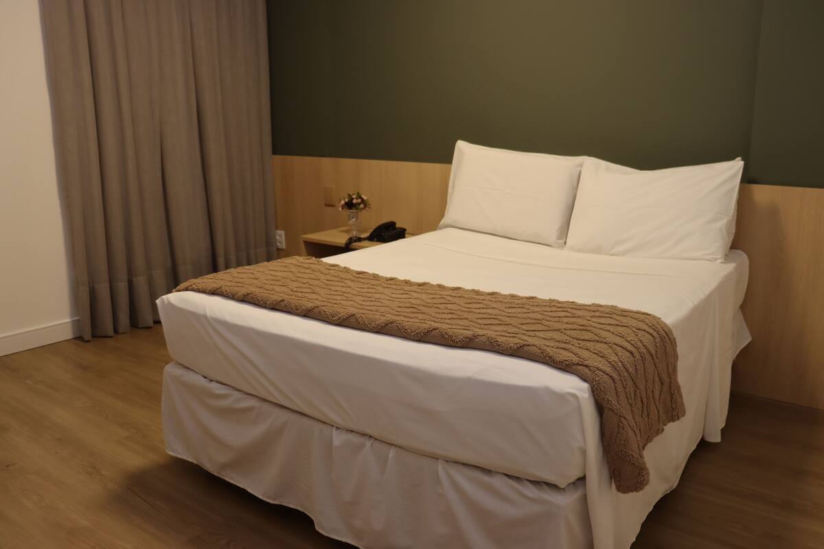 Een hotelkamer met een groot bed, een nachtkastje, een lamp en een gordijn.