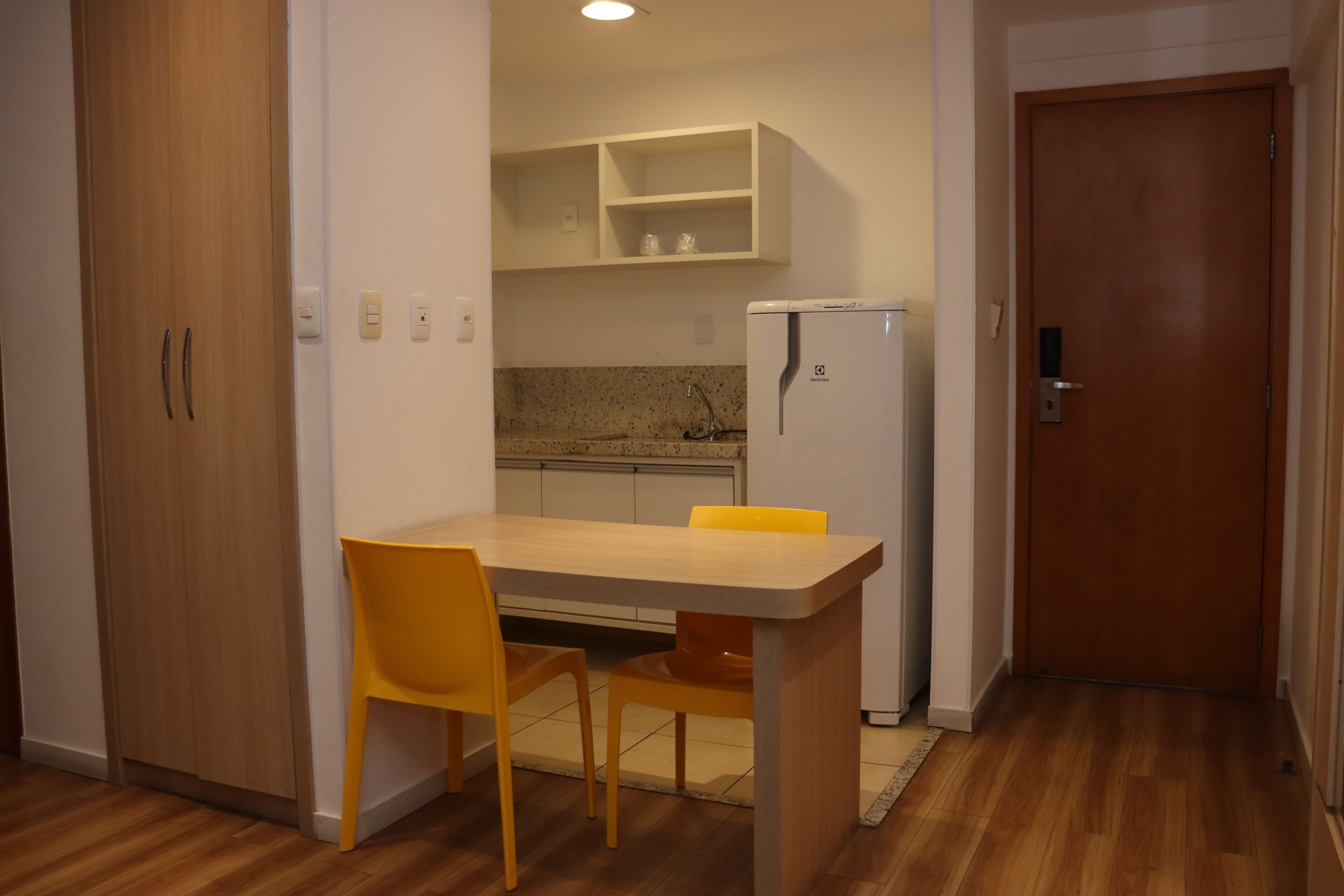 A compact kitchen with a dining table and chairs, a refrigerator, and a wooden door.