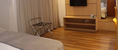 Habitación de hotel con cama, televisor montado en la pared, piso de madera y ventana con cortinas.