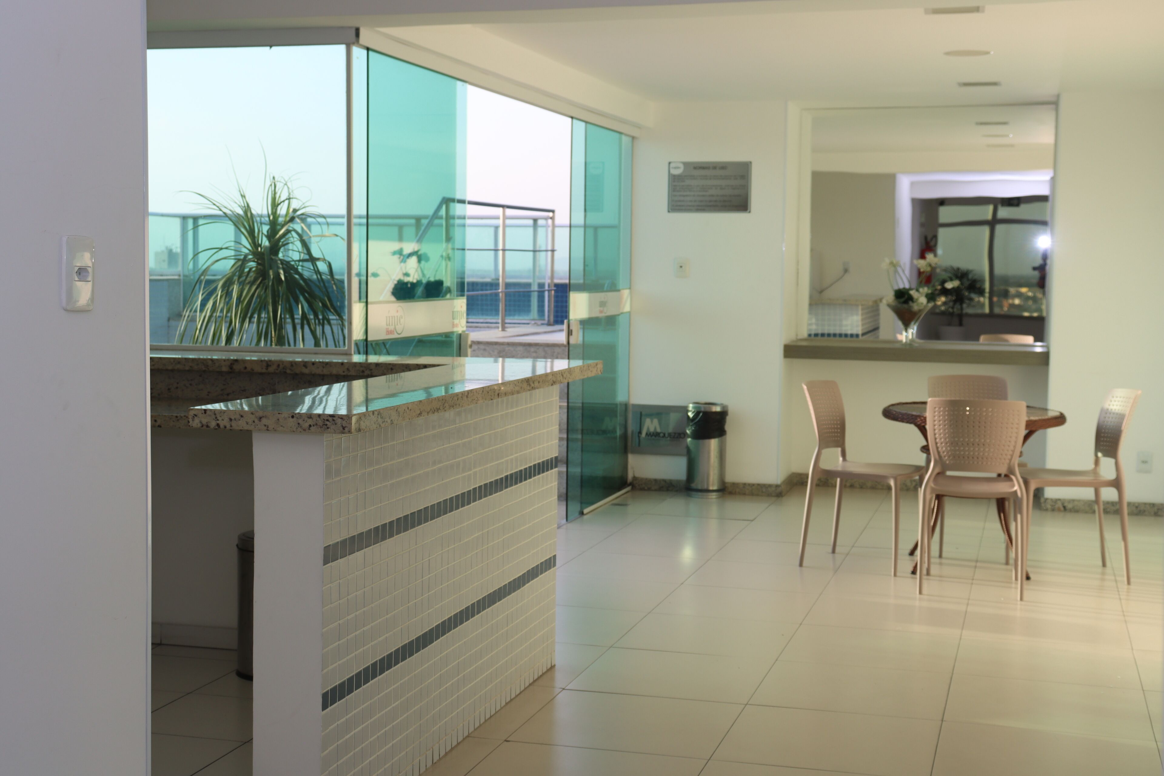 Una cocina moderna con un separador de vidrio, una zona de comedor con sillas y un cubo de basura.