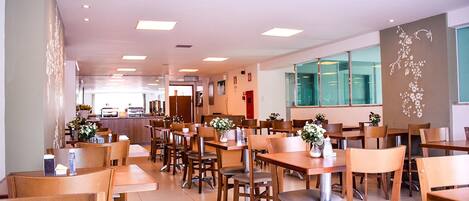 A spacious restaurant with wooden tables and chairs, a counter area, and large windows.