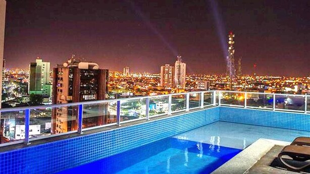 A rooftop pool with a cityscape view at night. - Único Apart Hotel (Feira de Santana)