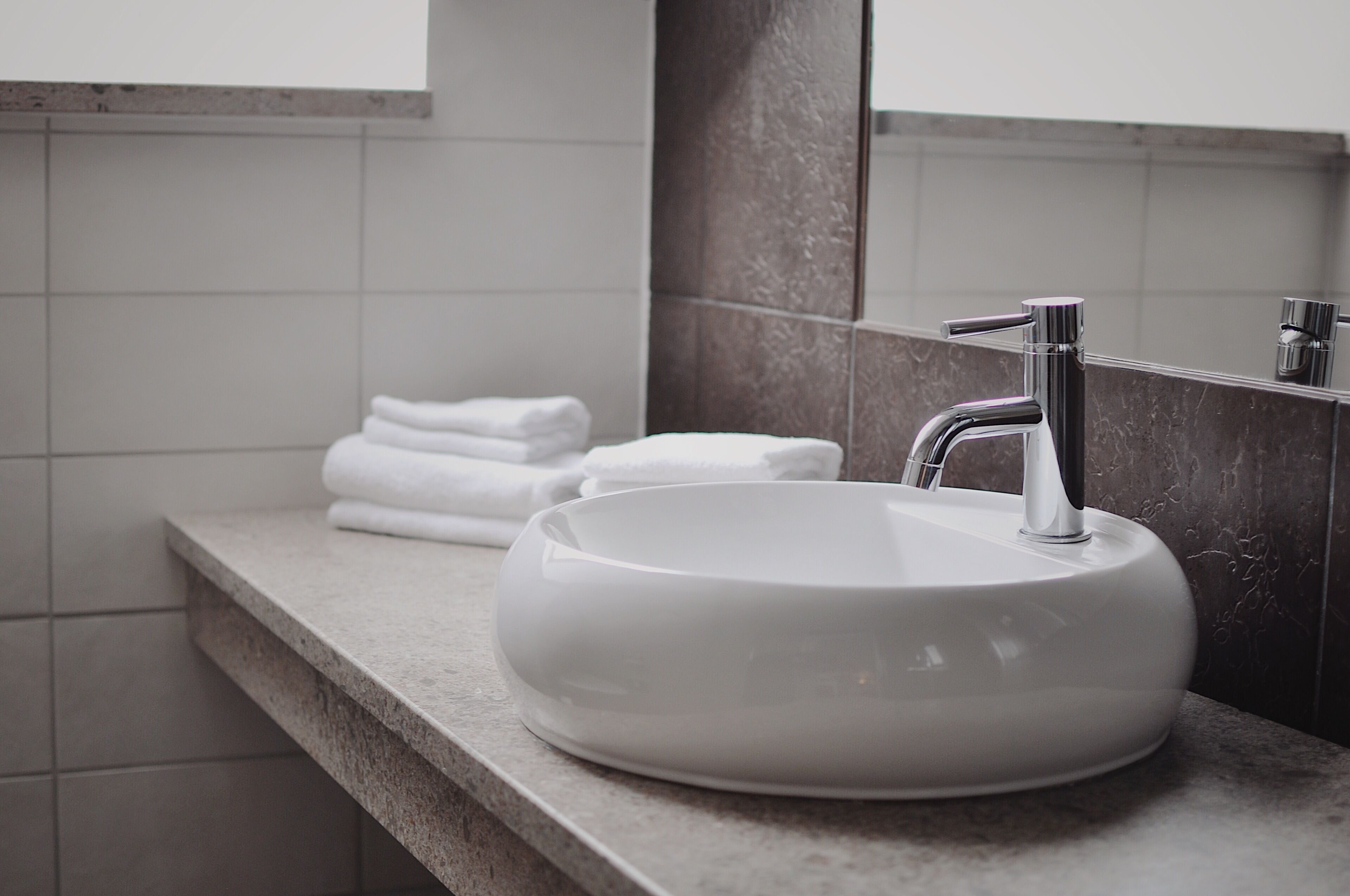 A modern bathroom with a round white sink, a mirror, and neatly stacked white towels.