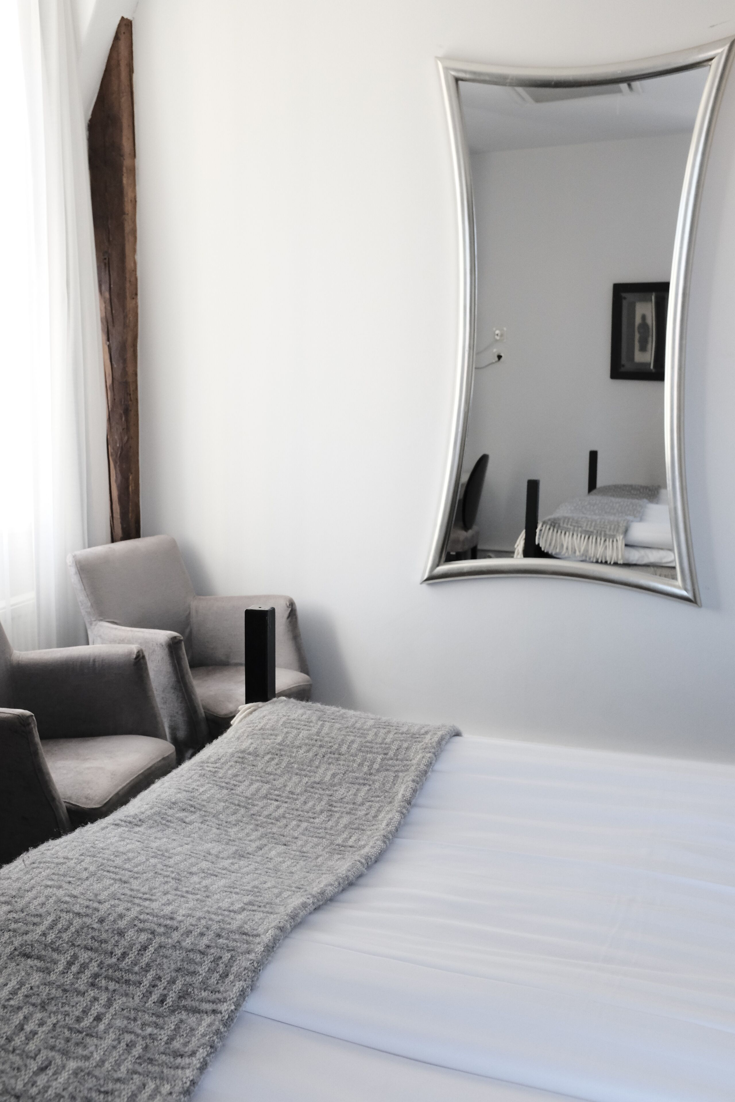 A hotel room with a bed, a large mirror, a chair, and a small table.