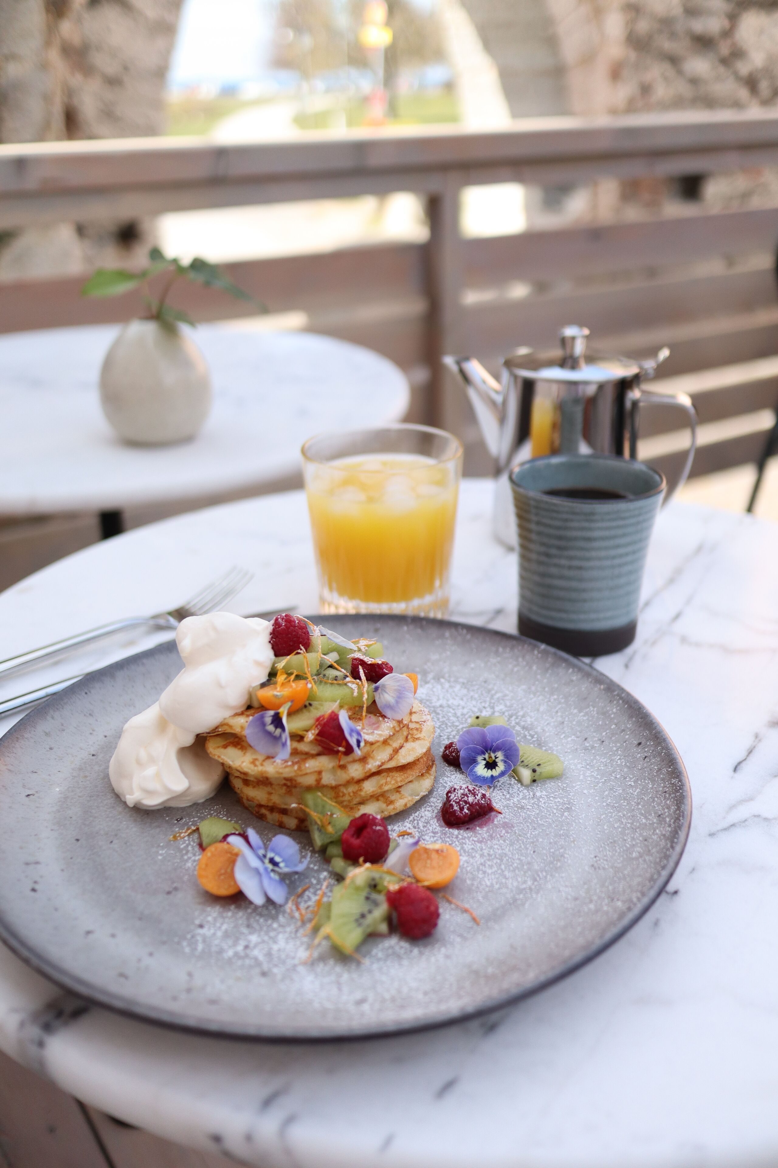 A breakfast setting with pancakes, fruit, and a pitcher of coffee on a table.