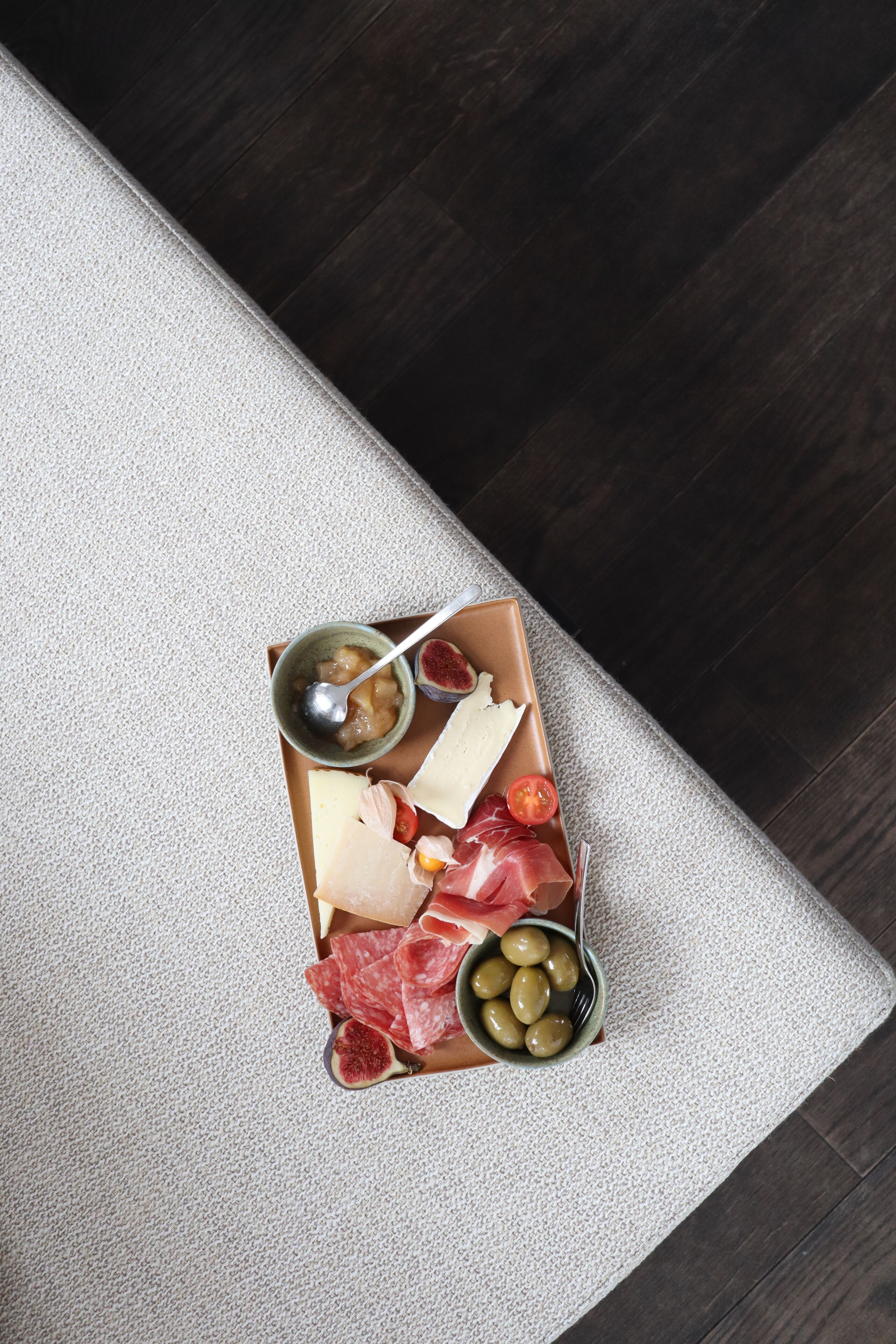 A box of assorted cheeses, meats, and olives on a textured surface.