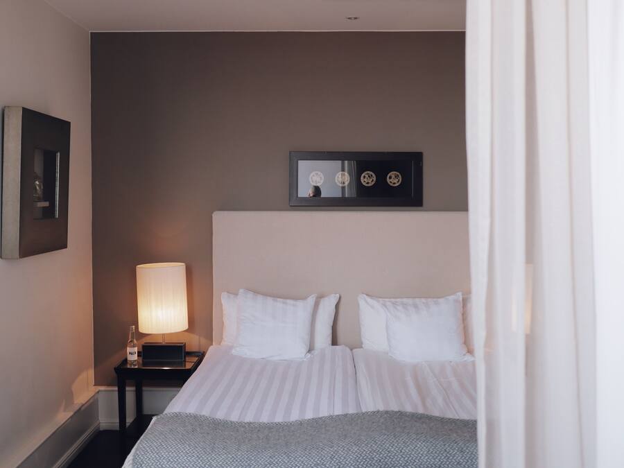 A hotel room with a bed, a nightstand with a lamp, and a framed picture on the wall.