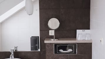 Une salle de bain moderne avec un lavabo blanc, des murs recouverts de carreaux foncés, des toilettes et un petit miroir.