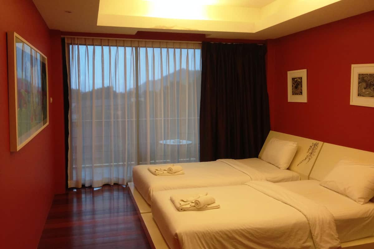 A hotel room with two beds, a large window with curtains, and a painting on the wall.