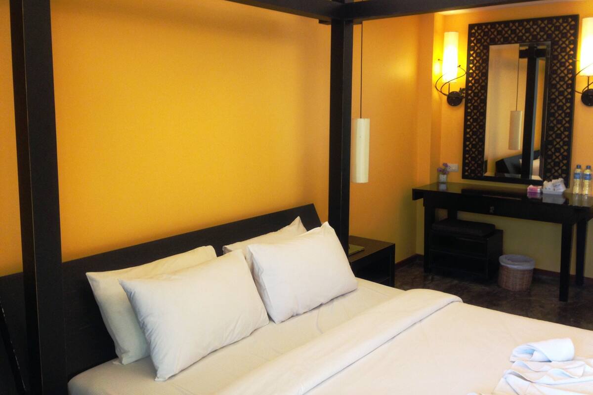 A hotel room with a bed, a nightstand, a mirror, and a desk with toiletries.