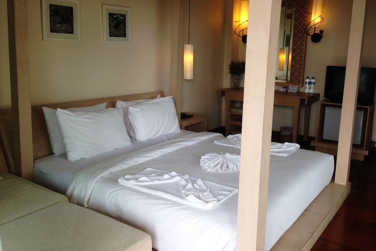 A hotel room with a large bed, a bedside table, a mirror, a television, and a small refrigerator.