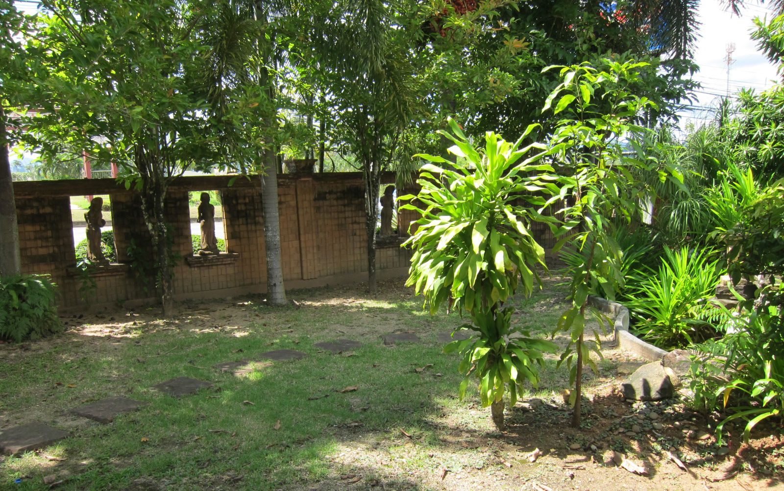 A garden with a variety of plants and a brick wall with statues.