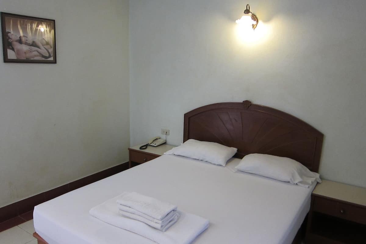 A neatly made bed with white linens and pillows, a bedside table with a lamp, and a framed picture on the wall.