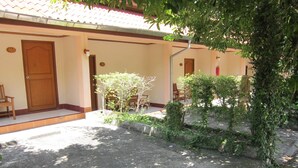 A building with numbered doors, a covered patio area with chairs, and a garden with plants and a small tree. - Oasis Resort (Krabi)