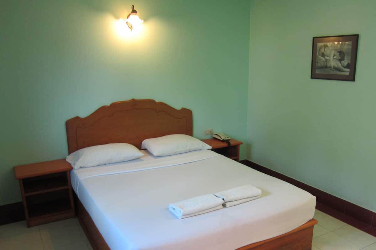 A neatly made bed with white linens and pillows, a wooden headboard, a bedside table with a lamp, and a framed picture on the wall.