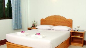 A neatly made bed with white linens and two towels, a wooden headboard, a bedside table with a phone and a book, and a window with curtains. - Oasis Resort (Krabi)