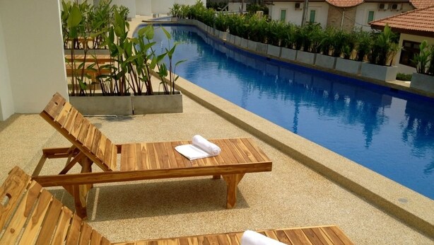 Due poltrone in legno con asciugamani, una piscina e vegetazione circostante.