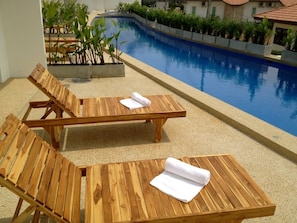 Dos sillones de madera con toallas, una piscina y follaje circundante.