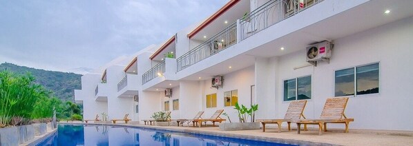 Un hotel moderno con piscina, varios balcones y sillones de descanso.