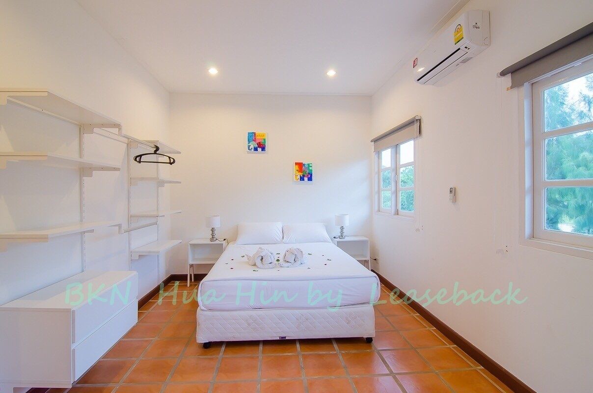 A bedroom with a bed, white walls, a window, and a shelf unit.