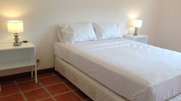 Habitación con cama individual, ropa de cama blanca, dos mesitas de noche con lámparas y suelo de baldosas.