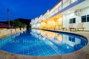 A swimming pool with lounge chairs and a building with balconies.