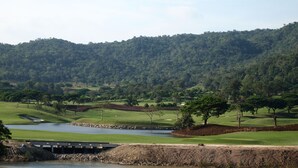 Un campo da golf con un ponte su una distesa d'acqua, circondato da dolci colline verdi.