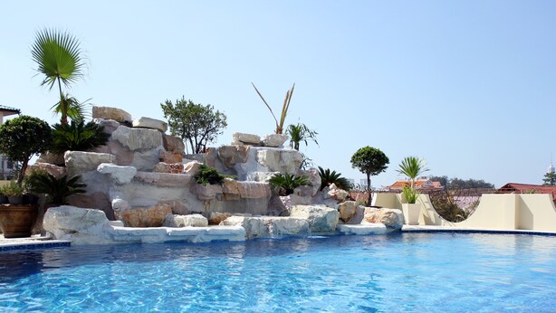 A swimming pool with clear blue water, surrounded by rock formations and palm trees. - LK Crystal Place (Pattaya)