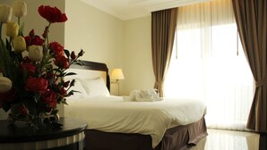 A hotel room with a neatly made bed, a vase of flowers on a side table, and a window with curtains. - LK Crystal Place (Pattaya)